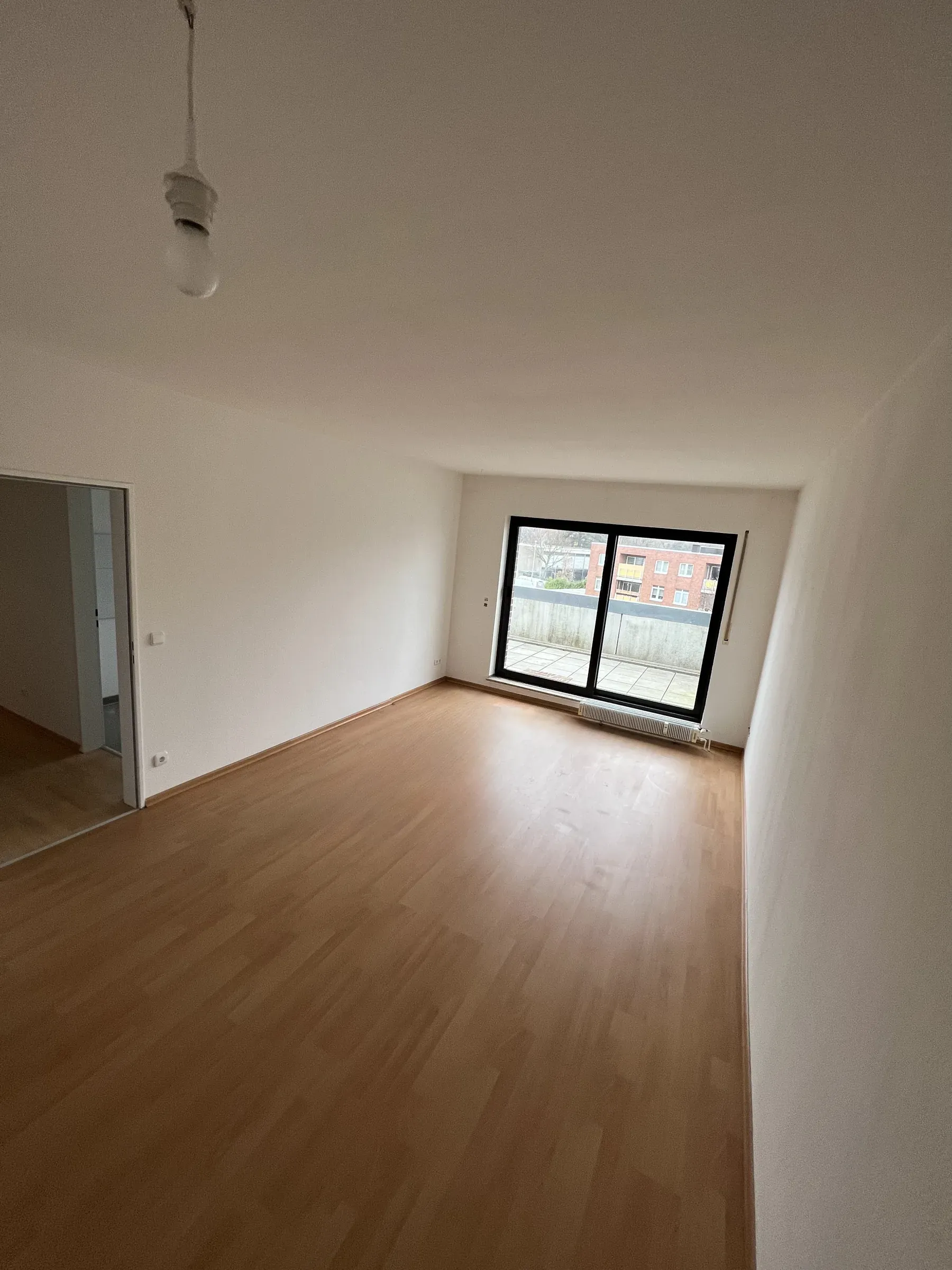 Leerstehendes Wohnzimmer mit hellem Holzboden, weiß gestrichenen Wänden und einem breiten Fenster