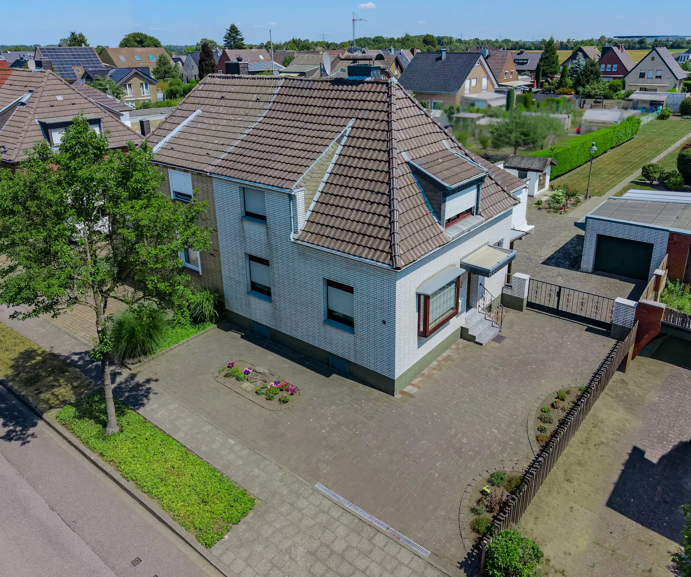 Haus mit hohem Walmdach und hellblau-grauer Fassade in Ecklage, davor gepflasterter Vorplatz
