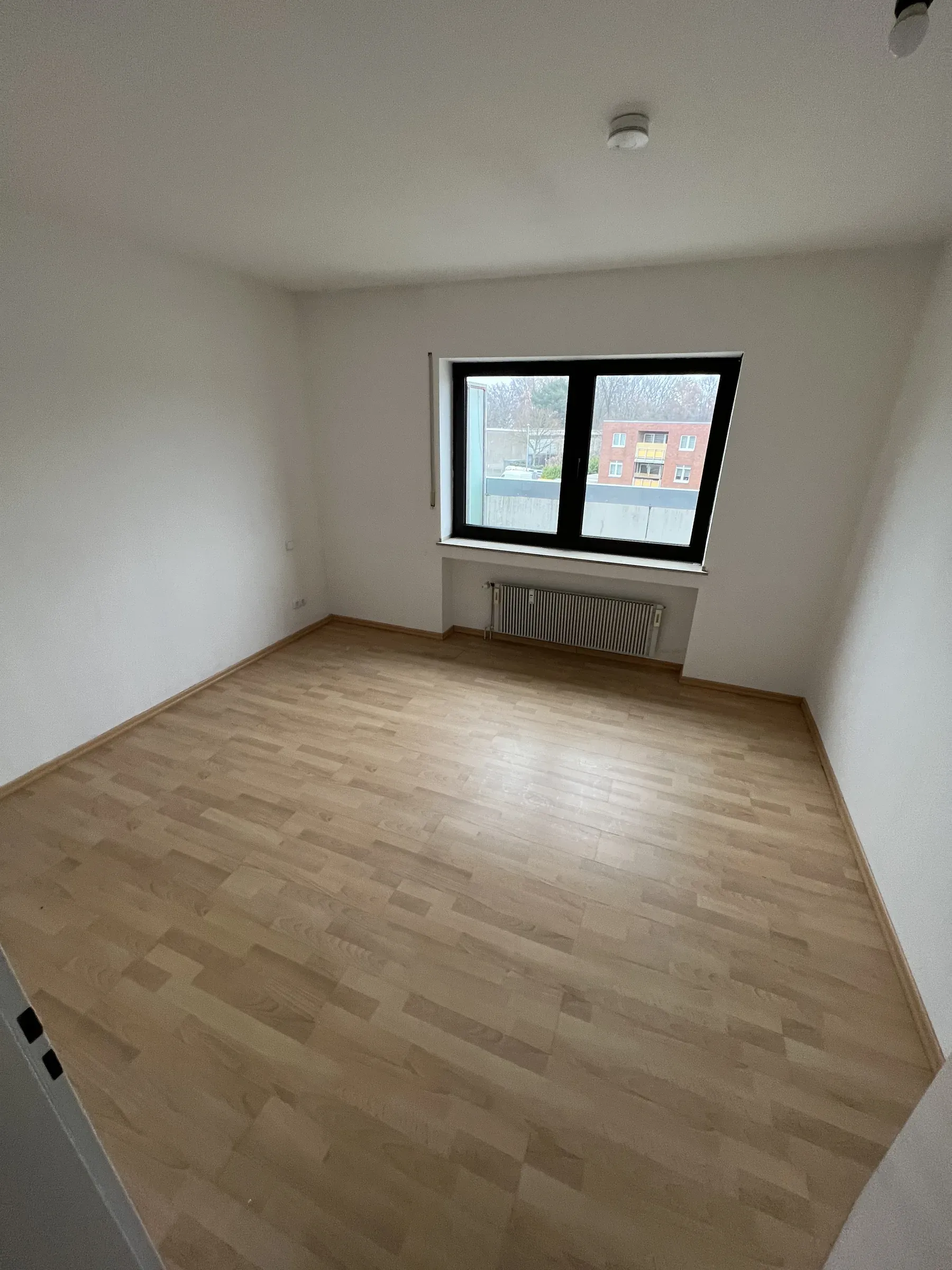 Zweiter Wohnraum mit Holzboden, Fenster und Heizkörper unter der Fensterbank