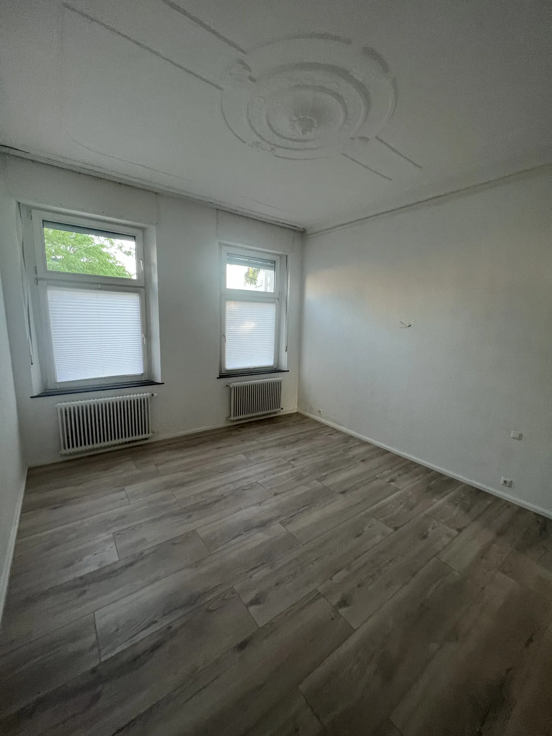 Zimmer mit erhaltener Stuckrosette an der Decke und zwei Fenstern zur ruhigen Seite
