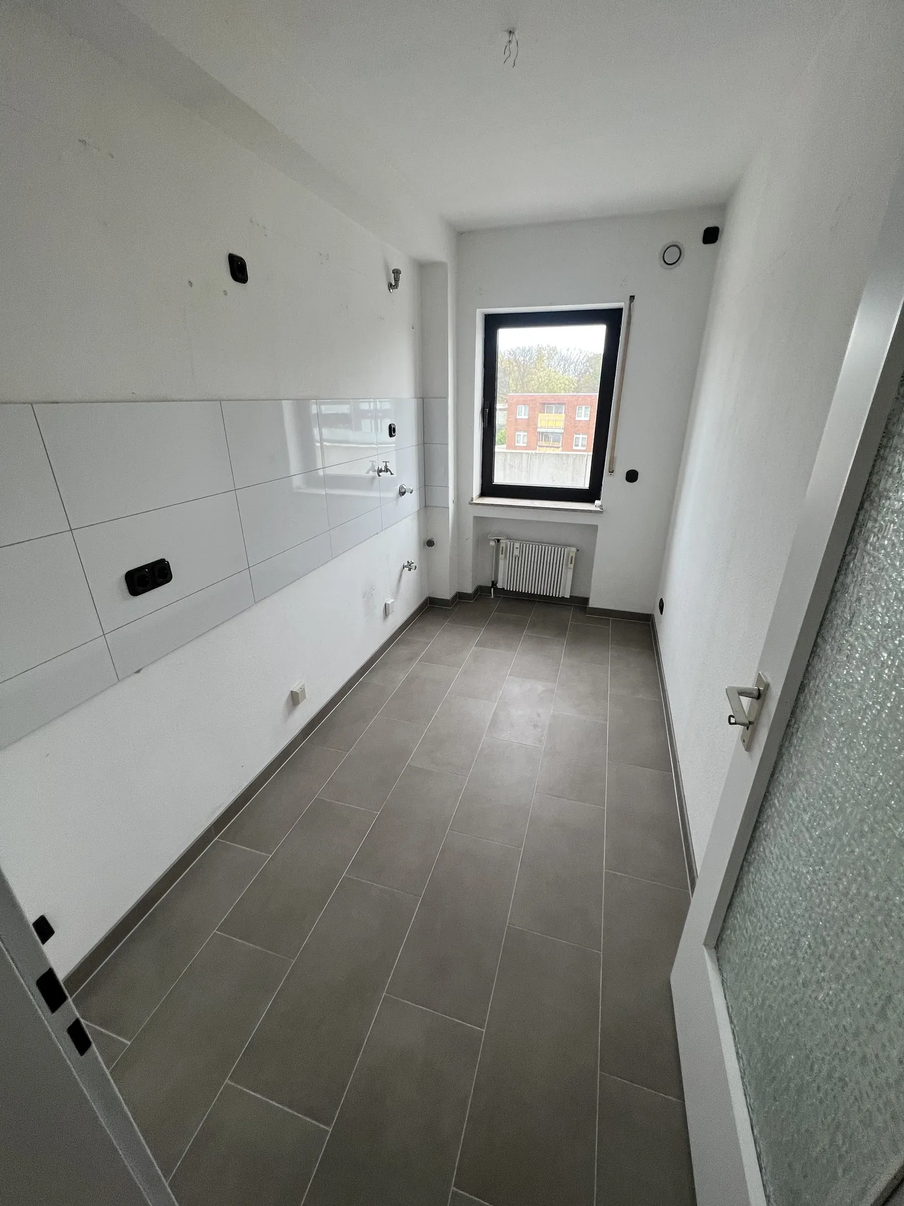 Küche mit weißem Fliesenspiegel, dunklem Fliesenboden und Fenster zum Hof