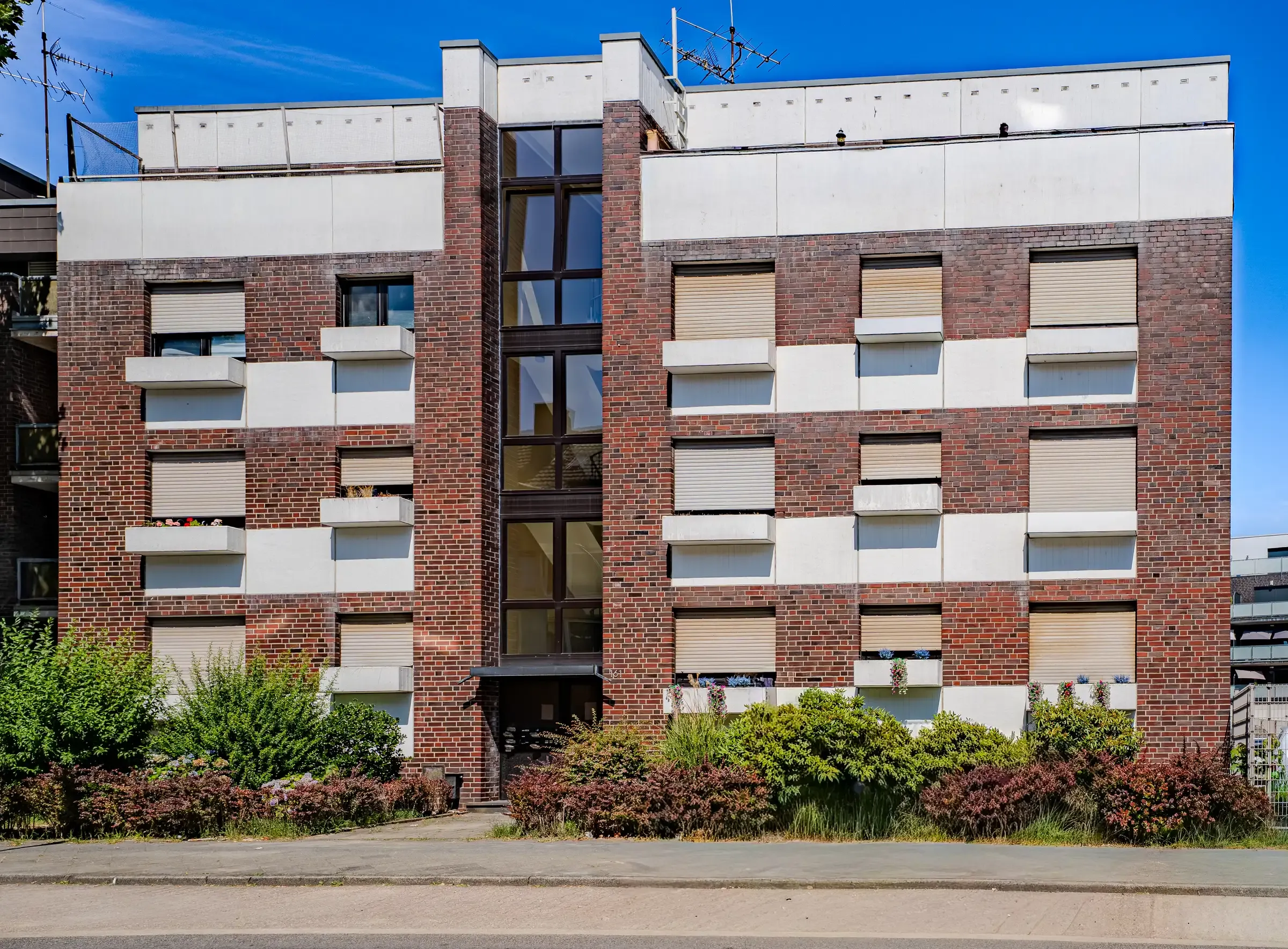 Straßenansicht schräg von rechts mit bepflanztem Vorgartenstreifen