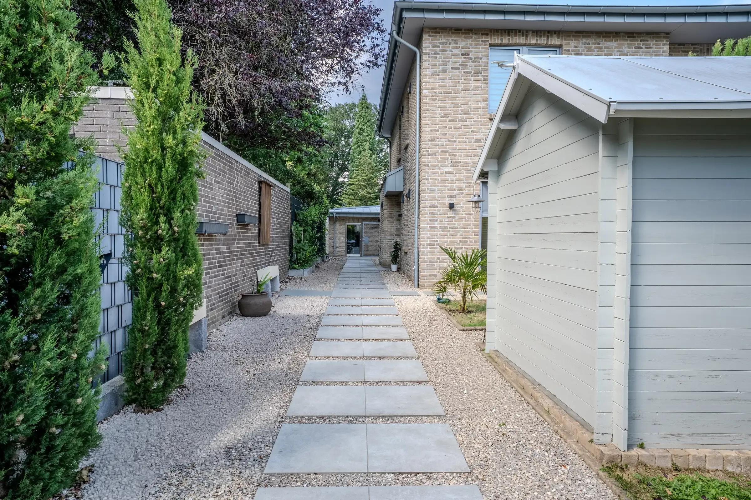 Plattenweg zwischen Säulenzypressen und Garage Richtung Hauseingang